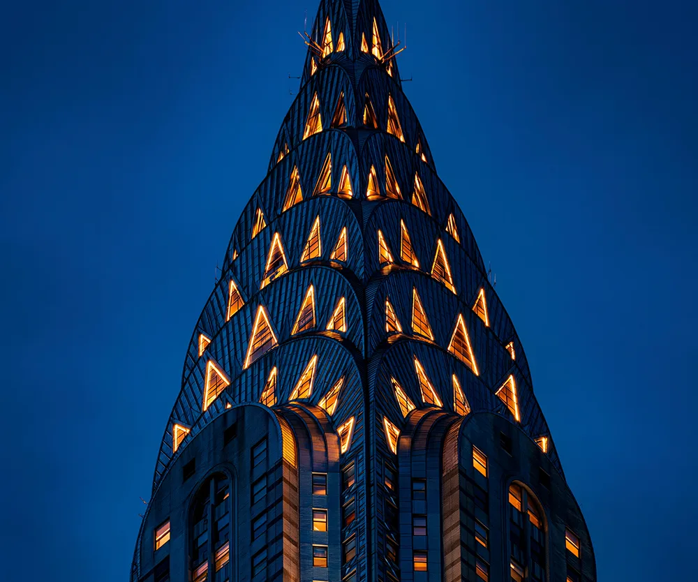 The Chrysler Building's Art Deco crown illuminated with triangular lights against a deep blue night sky