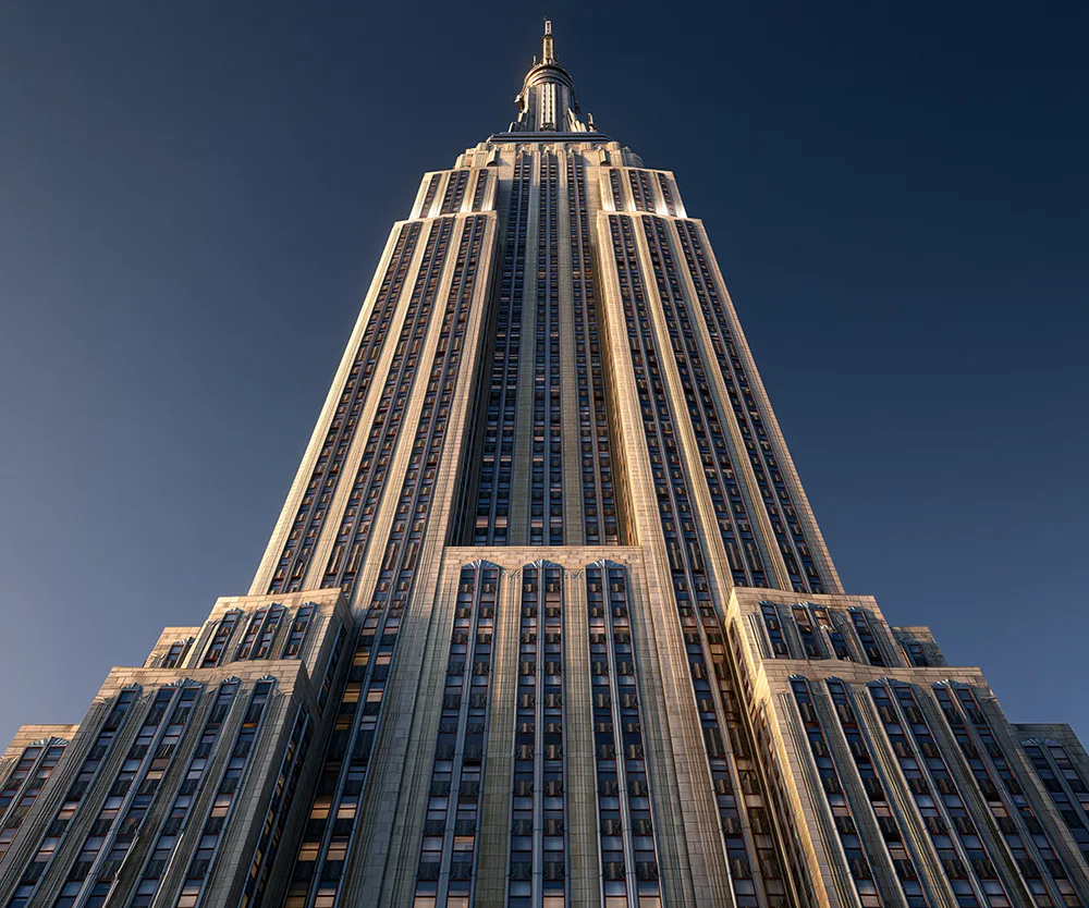 Looking up at the Empire State Building's Art Deco setbacks and mast against a blue sky